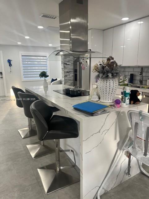 kitchen with island exhaust hood, a breakfast bar, white cabinetry, high end refrigerator, and sink