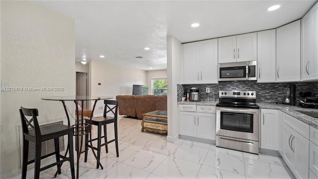 kitchen with backsplash, white cabinetry, light stone counters, and appliances with stainless steel finishes