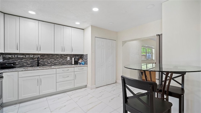 kitchen featuring light stone countertops, backsplash, white cabinetry, and sink