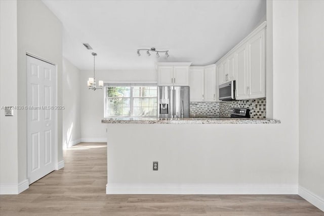 kitchen with hanging light fixtures, tasteful backsplash, appliances with stainless steel finishes, white cabinets, and light wood-type flooring