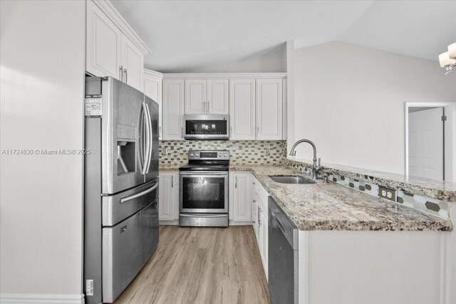 kitchen with light stone counters, stainless steel appliances, vaulted ceiling, sink, and white cabinets