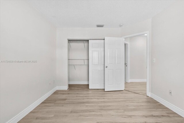 unfurnished bedroom featuring a textured ceiling, light hardwood / wood-style flooring, and a closet