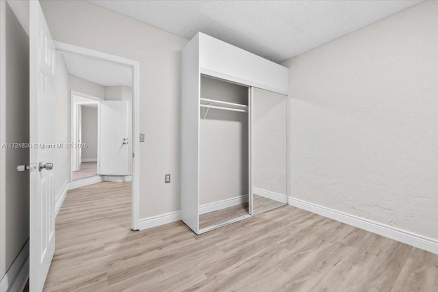 unfurnished bedroom with light wood-type flooring, a textured ceiling, and a closet