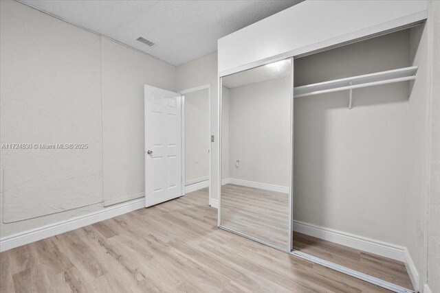 unfurnished bedroom featuring light wood-type flooring, a textured ceiling, and a closet