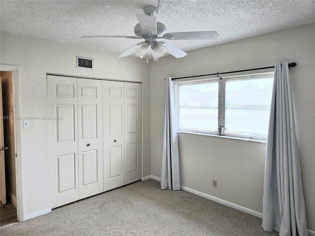 unfurnished bedroom with a textured ceiling, ceiling fan, light carpet, and a closet