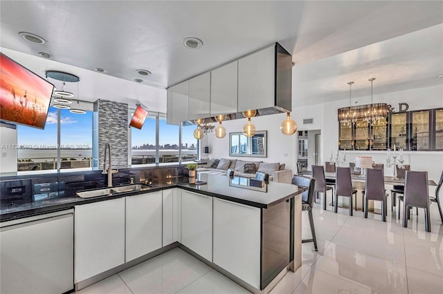 kitchen with dark countertops, dishwasher, a sink, light tile patterned flooring, and a chandelier