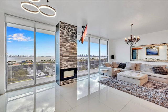 tiled living room with a large fireplace, a water view, a chandelier, and a wall of windows