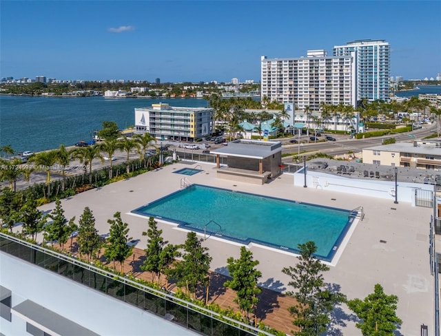 community pool with a water view, a patio area, and a view of city