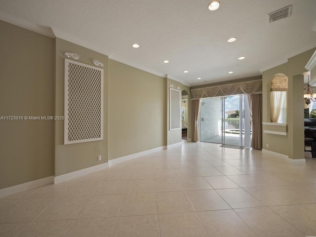 empty room featuring a textured ceiling, light tile patterned floors, and crown molding