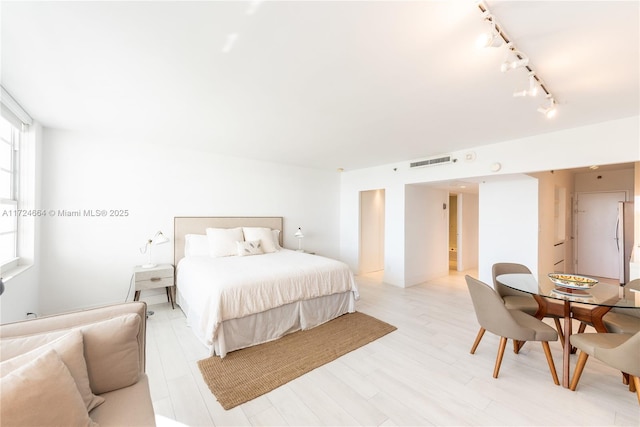 bedroom with rail lighting, stainless steel refrigerator, and light hardwood / wood-style flooring