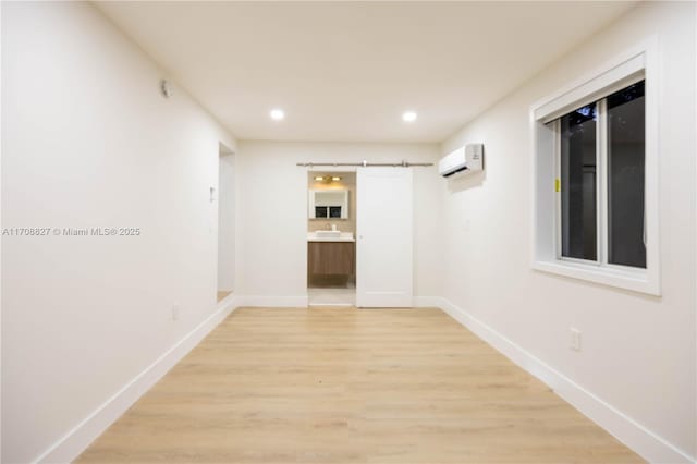spare room featuring a barn door, light hardwood / wood-style floors, and a wall mounted AC