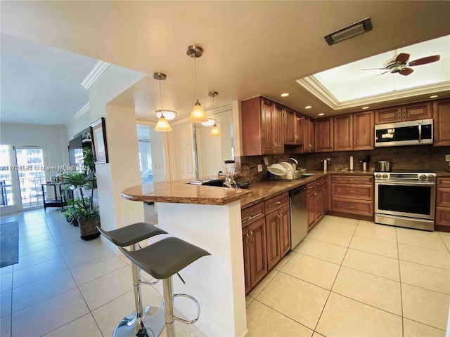 kitchen featuring a kitchen bar, kitchen peninsula, ornamental molding, stainless steel appliances, and hanging light fixtures