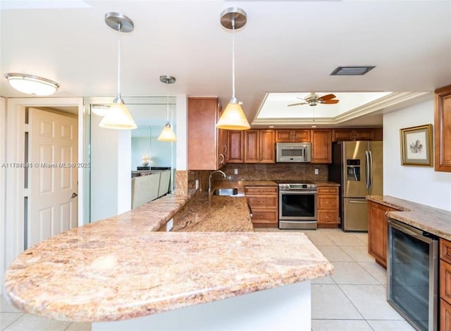 kitchen with hanging light fixtures, appliances with stainless steel finishes, a tray ceiling, kitchen peninsula, and beverage cooler