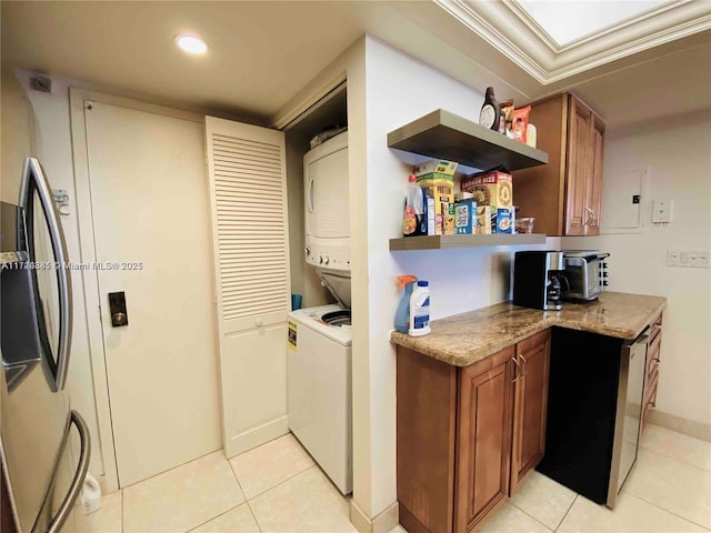 laundry area featuring stacked washer / drying machine, light tile patterned flooring, and ornamental molding