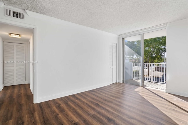 empty room with a textured ceiling, a wall of windows, and dark wood-type flooring