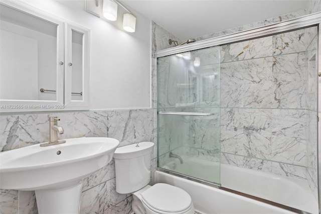 full bathroom featuring tile walls, bath / shower combo with glass door, toilet, and sink