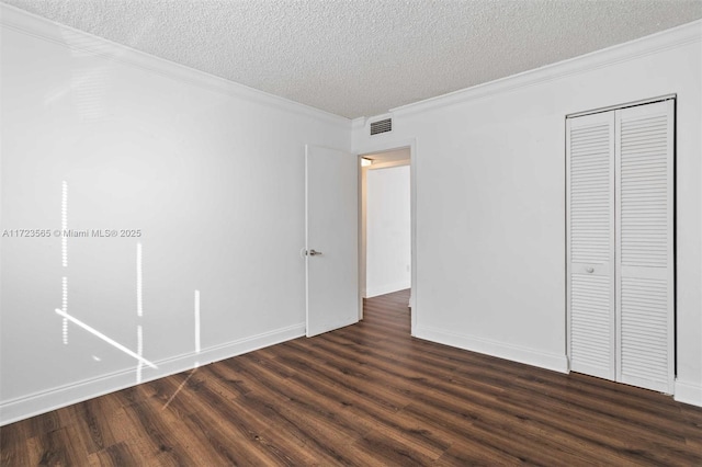 unfurnished bedroom featuring a textured ceiling, dark wood-type flooring, ornamental molding, and a closet