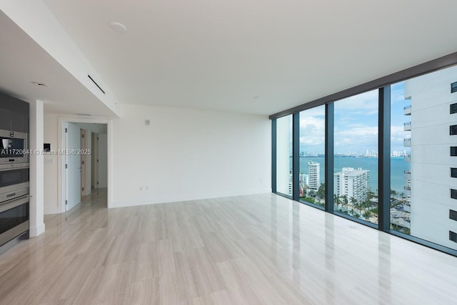 empty room featuring expansive windows, light hardwood / wood-style flooring, and a water view