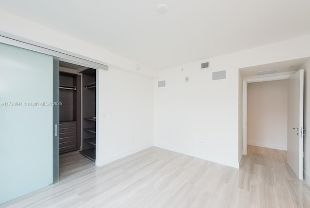 unfurnished bedroom featuring a walk in closet, a closet, and light hardwood / wood-style floors