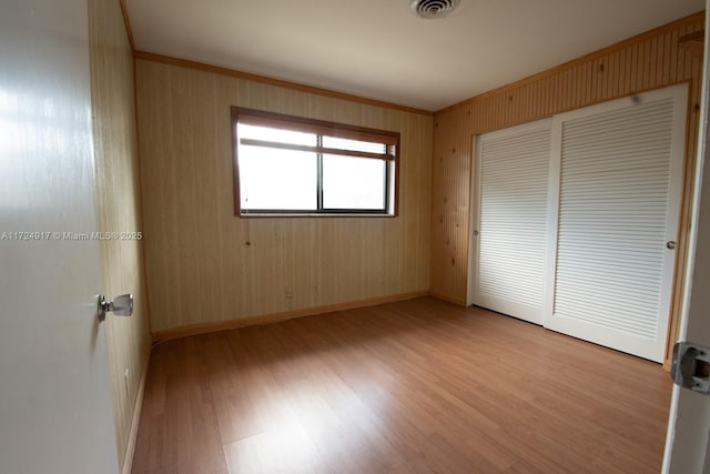 unfurnished bedroom featuring wood walls, a closet, and light wood-type flooring