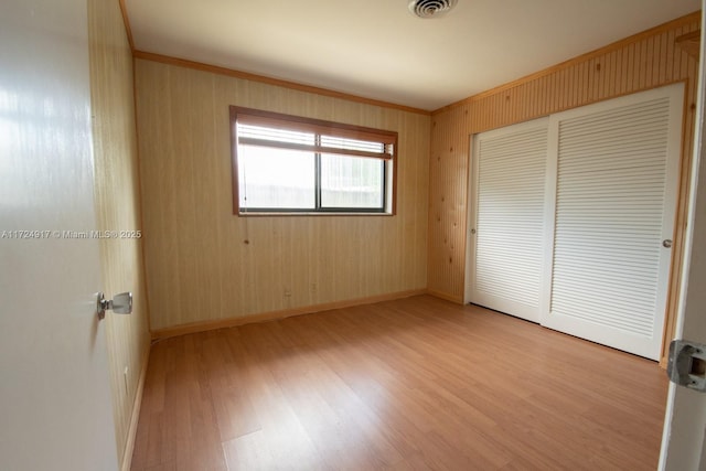 unfurnished bedroom with wooden walls, a closet, and light hardwood / wood-style flooring