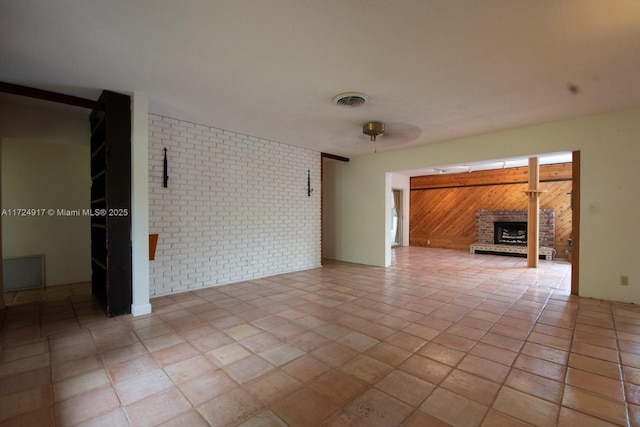 unfurnished living room with a brick fireplace, ceiling fan, and wood walls