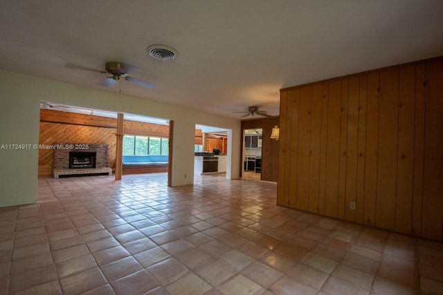 unfurnished living room with light tile patterned floors, a brick fireplace, ceiling fan, and wooden walls