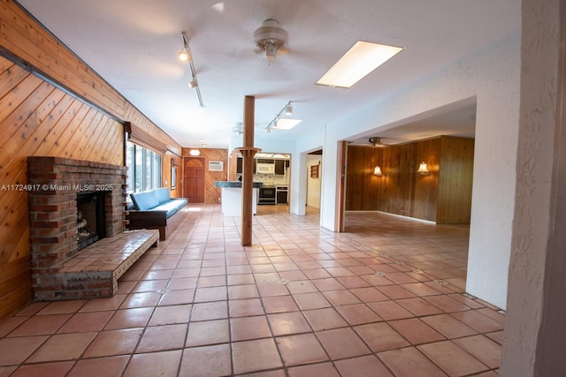 unfurnished living room with rail lighting, ceiling fan, light tile patterned floors, a fireplace, and wood walls