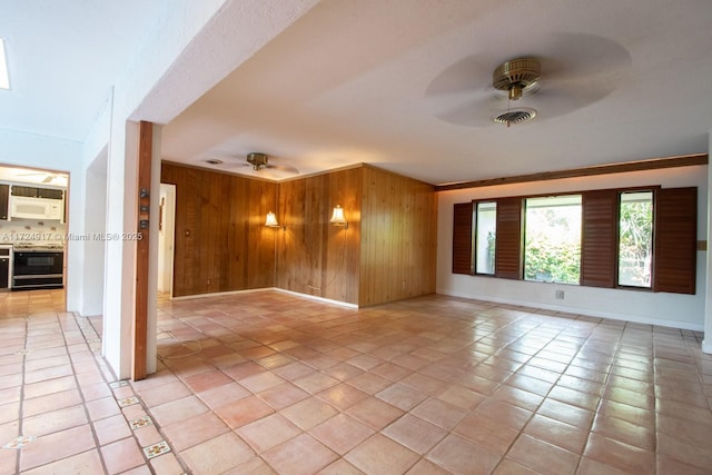 empty room with wooden walls, ceiling fan, light tile patterned floors, and ornamental molding