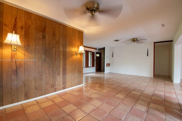 spare room with crown molding, ceiling fan, wooden walls, and brick wall