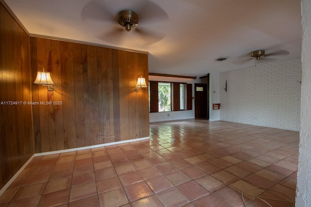 tiled empty room featuring brick wall, ceiling fan, ornamental molding, and wood walls