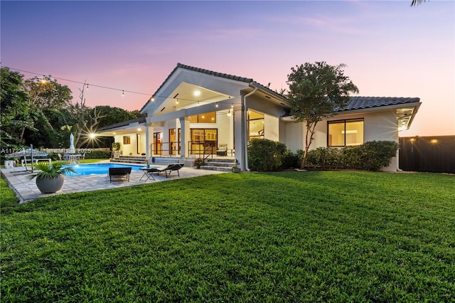 back house at dusk with a patio area and a lawn