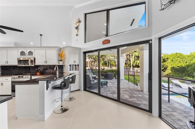 kitchen with appliances with stainless steel finishes, ceiling fan, white cabinets, and backsplash