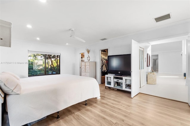 bedroom with ornamental molding, light wood-type flooring, a closet, and a spacious closet