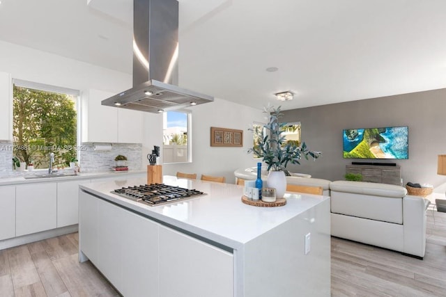 kitchen with island exhaust hood, a center island, stainless steel gas stovetop, sink, and white cabinetry