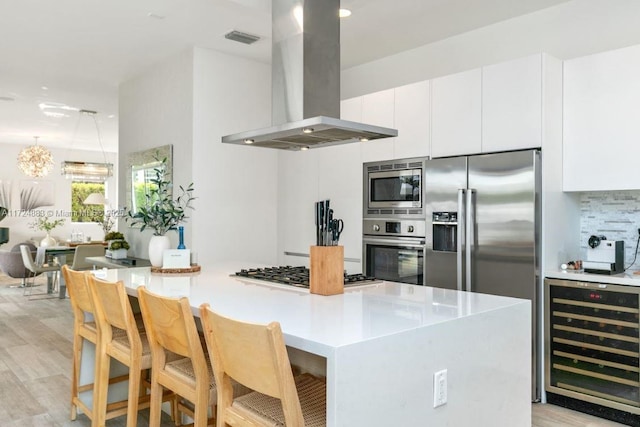 kitchen featuring appliances with stainless steel finishes, beverage cooler, island exhaust hood, and white cabinetry