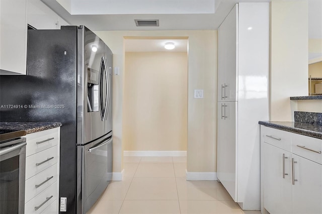 kitchen featuring white cabinetry, light tile patterned floors, dark stone counters, and appliances with stainless steel finishes