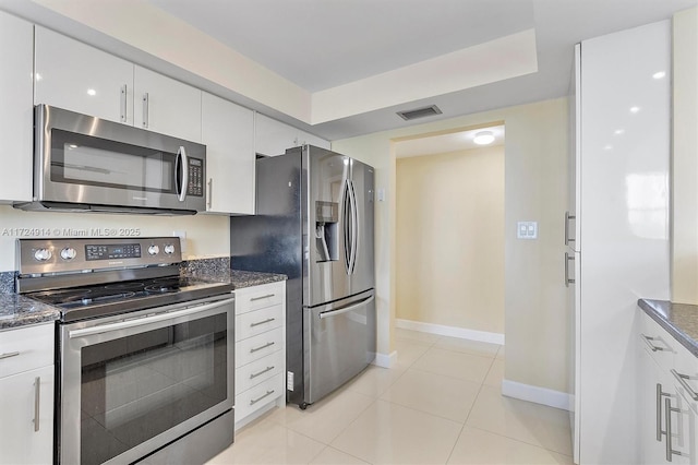 kitchen featuring stainless steel appliances, white cabinetry, light tile patterned floors, and dark stone counters