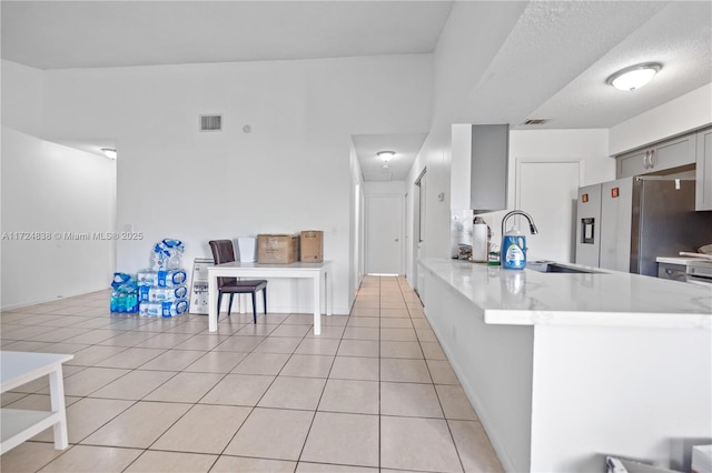 kitchen with kitchen peninsula, a textured ceiling, sink, stainless steel fridge with ice dispenser, and light tile patterned flooring