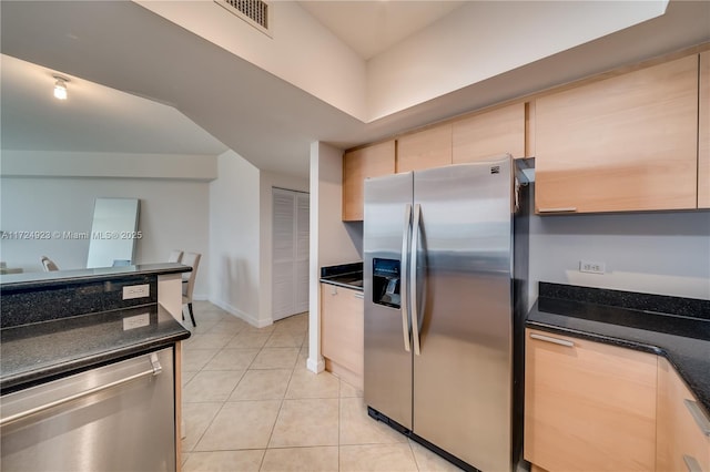 kitchen featuring light brown cabinetry, light tile patterned floors, dark stone counters, and appliances with stainless steel finishes