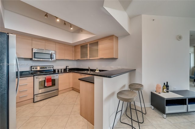 kitchen featuring a breakfast bar area, kitchen peninsula, light brown cabinetry, and stainless steel appliances