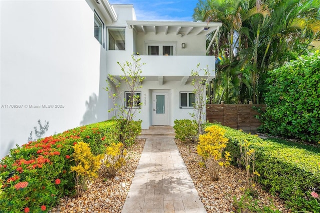 entrance to property featuring a balcony, fence, and stucco siding