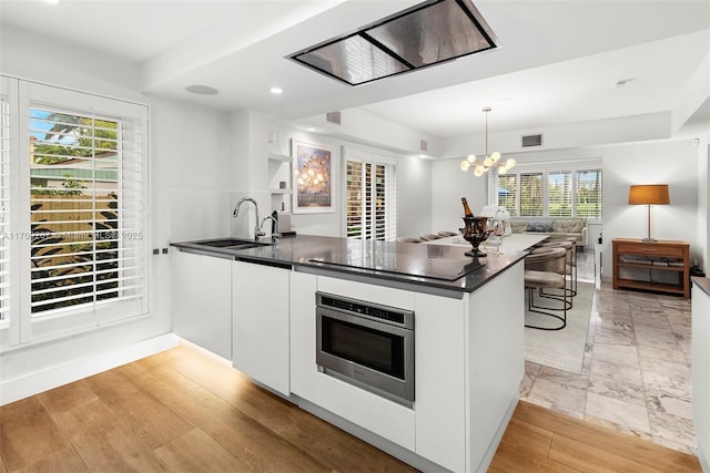 kitchen with visible vents, a sink, dark countertops, open floor plan, and white cabinetry