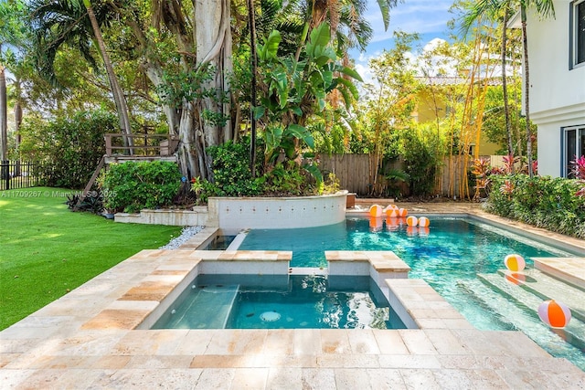 view of pool with a yard, fence, and a pool with connected hot tub