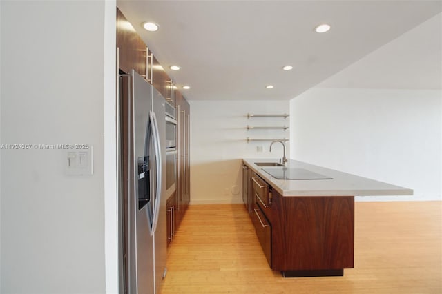 kitchen with sink, a kitchen breakfast bar, light hardwood / wood-style flooring, kitchen peninsula, and appliances with stainless steel finishes