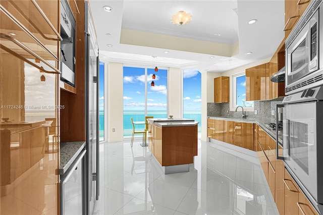 kitchen with a water view, a tray ceiling, oven, and a center island