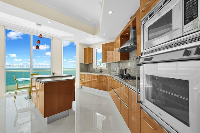 kitchen featuring a center island, sink, stainless steel appliances, a water view, and wall chimney exhaust hood