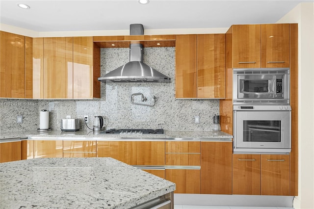 kitchen with light stone countertops, appliances with stainless steel finishes, decorative backsplash, and wall chimney range hood