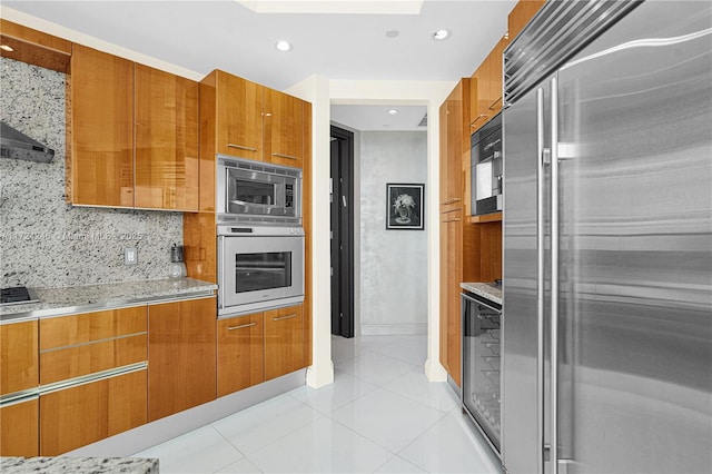 kitchen with a skylight, built in appliances, backsplash, light tile patterned flooring, and light stone counters