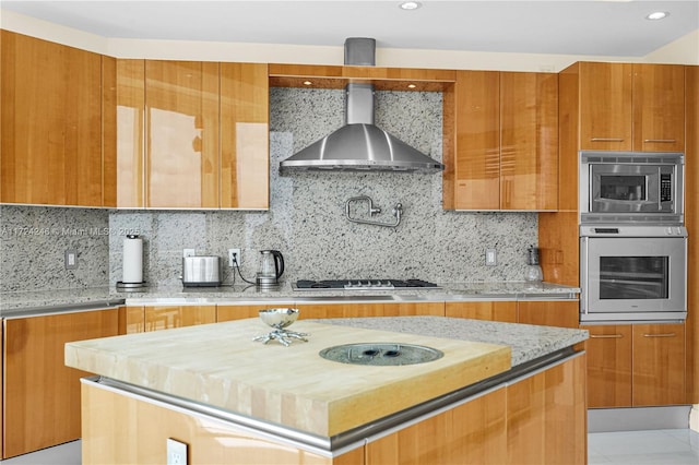 kitchen with tasteful backsplash, wooden counters, a center island, stainless steel appliances, and wall chimney exhaust hood